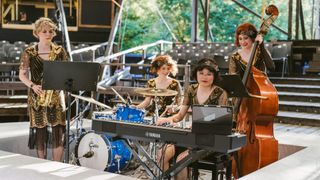 Eine Frau in einem Flitterkleid spielt eine Yamaha-Tastatur bei einem Open-Air-Konzert mit einer Schlagzeugerin und einer Cellistin im Hintergrund.