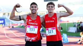 Zwei Athleten, einer mit einem roten Trikot mit dem Wort Turkiye und der Nummer 151, der andere mit Osterreich und der Nummer 321, posieren fur ein Foto auf einer Bahn.