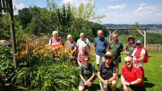 Eine Gruppe von Menschen, möglicherweise auf einer Wanderung, posiert für ein Foto in einem Garten mit bunten Blumen und Bäumen im Hintergrund.