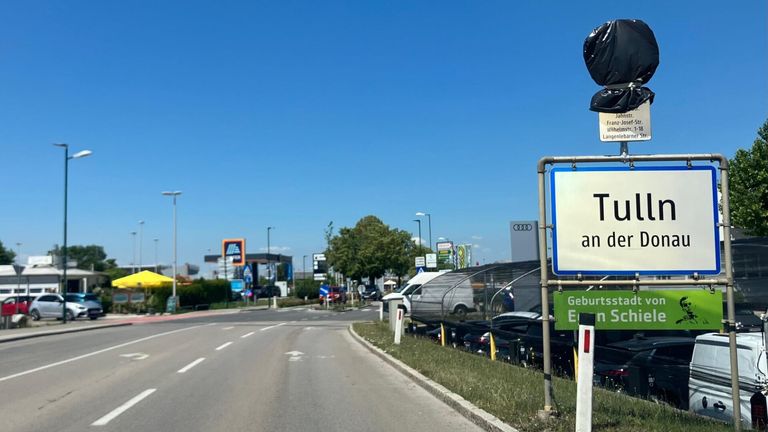 Eine Straße mit geparkten Autos in der Nähe einer Tankstelle. Ein Schild steht 'an' und ein grünes Schild steht 'Gebur E'.
