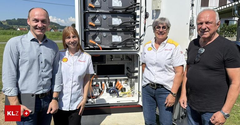Vier Mitarbeiter posieren vor einem elektrischen Gerätekasten. Der Kasten ist offen und enthält zahlreiche Kabel und Paneele.
