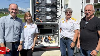 Vier Mitarbeiter posieren vor einem elektrischen Gerätekasten. Der Kasten ist offen und enthält zahlreiche Kabel und Paneele.