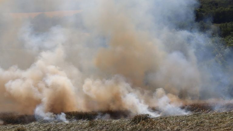 Ein großes Stück Land brennt und produziert dicken weißen und braunen Rauch. Das Feuer scheint trockenes Gras und Büsche zu konsumieren.