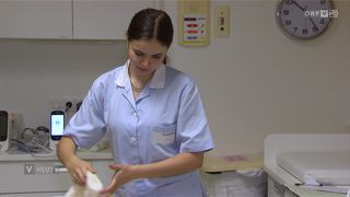 Eine Krankenschwester in blauer Kleidung arbeitet in einem Krankenhauszimmer und bereitet einen weißen Verband vor.