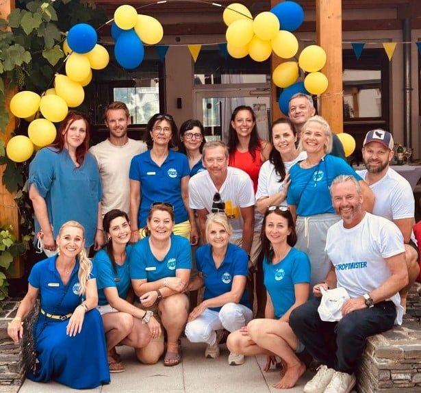 Eine Gruppe von Menschen in blauen und weißen Uniformen mit gelben Gürteln posiert für ein Foto vor einem Gebäude mit Luftballons und Pflanzen.