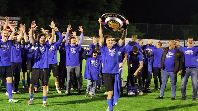 Eine Gruppe junger Männer in blauen Trikots feiert einen Sieg auf einem Feld, einer hält eine Trophäe.