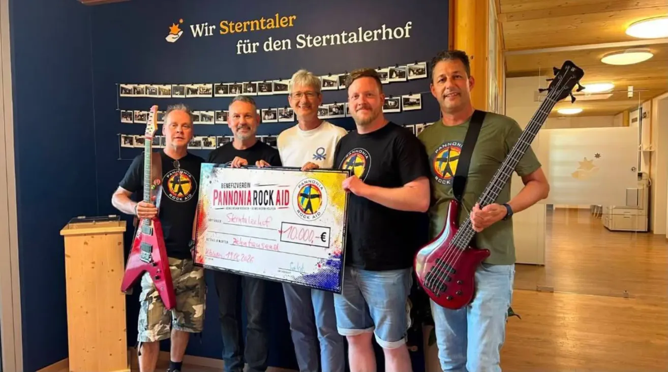 Fünf Männer posieren für ein Foto mit einem großen Scheck über 10.000 Euro. Sie halten Gitarren und stehen vor einer Wand mit Fotos und Text auf Deutsch.