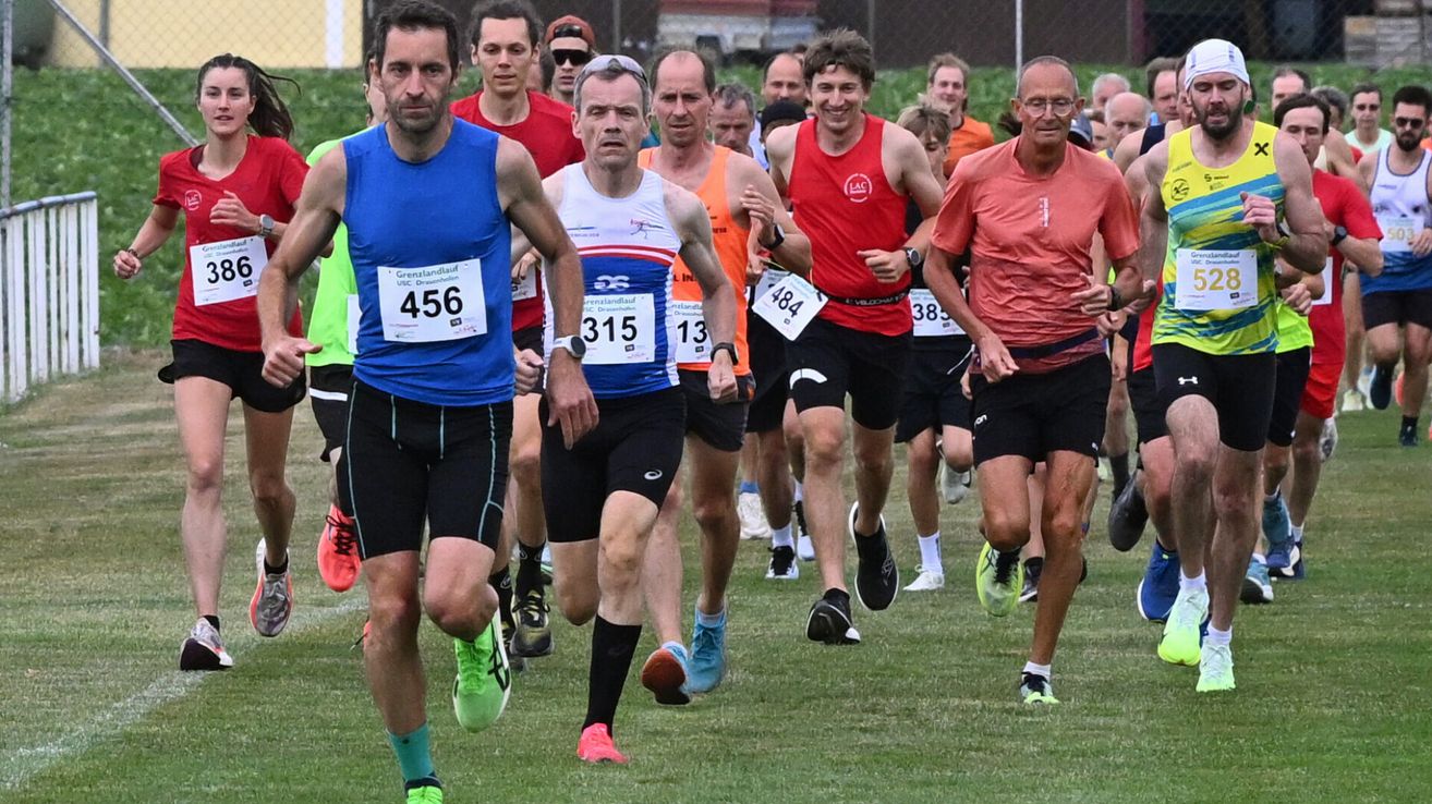 Several runners compete in a race. One runner wears a blue shirt with the number 456. Another wears a red shirt with the number 389.
