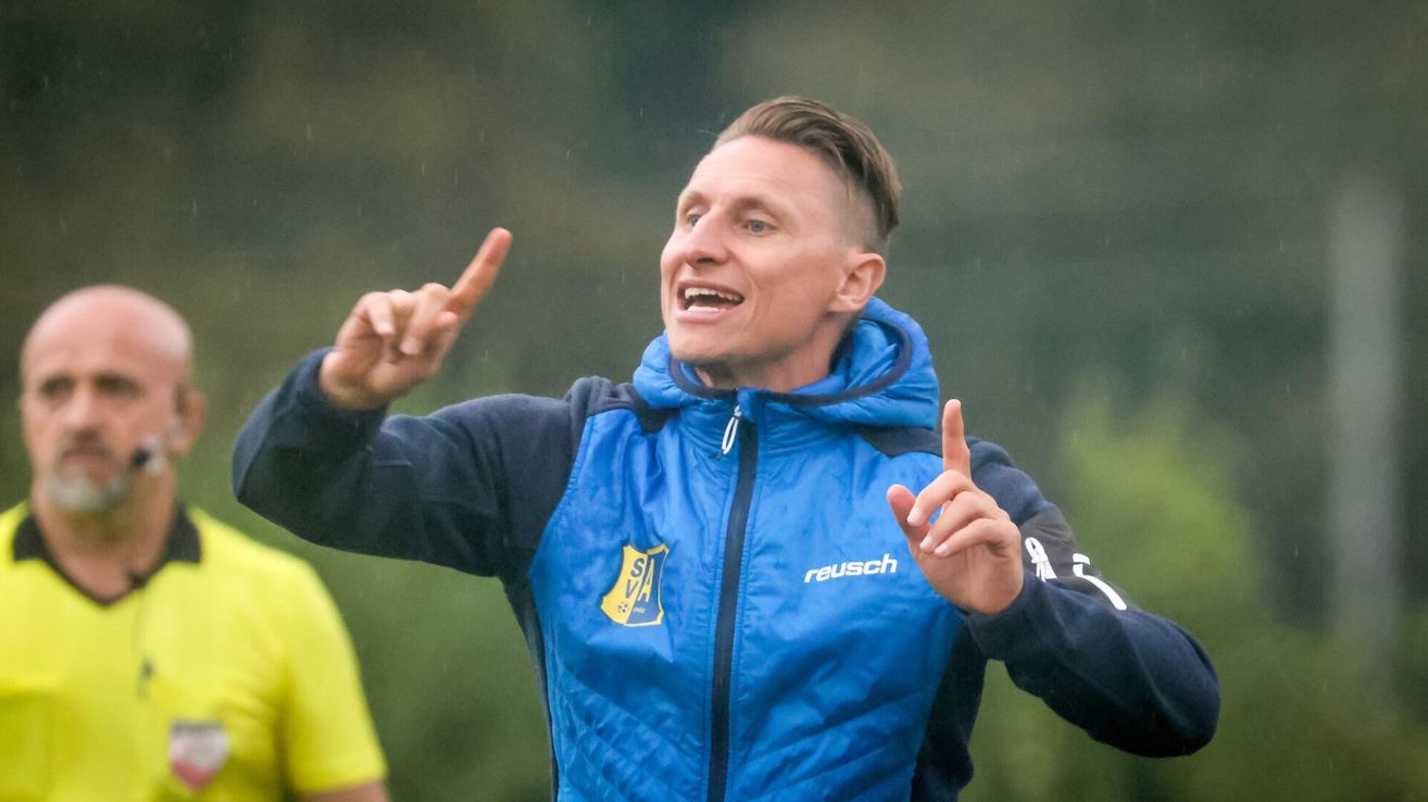 A man in a blue jacket smiles and points fingers while standing in the rain.