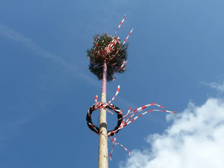 A tall wooden pole with a wreath and red and white ribbons attached to it is against a blue sky.