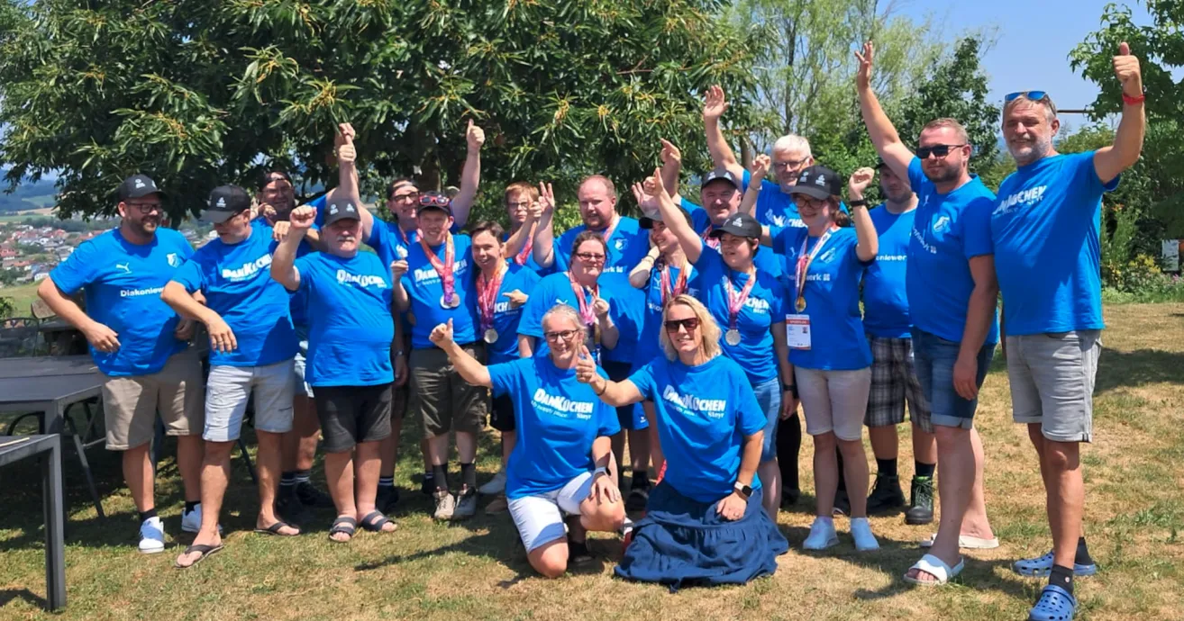 A group of people in blue shirts and glasses pose for a photo with raised hands, some wearing medals.