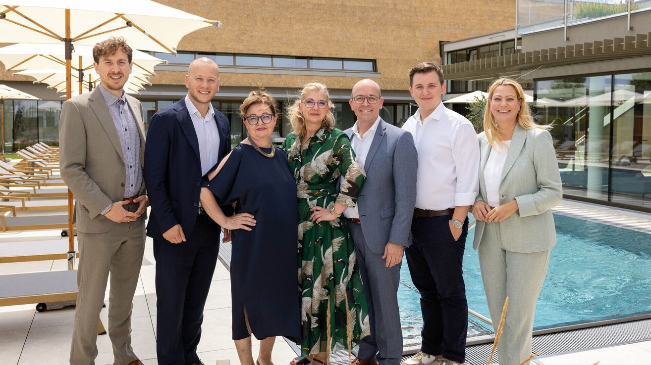 Eine Gruppe formell gekleideter Personen, sowohl Männer als auch Frauen, stehen am Pool, lächeln und posieren für ein Foto.