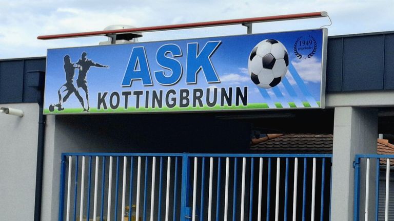 Ein großes blaues Schild mit den Worten Ask Kottingbrunn in weißen Buchstaben. Ein Fußball ist in der Luft über dem Schild.