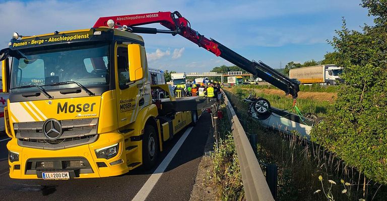 A large yellow truck is towing a car off the road. A crane is on the truck, and people are gathered around the vehicle.