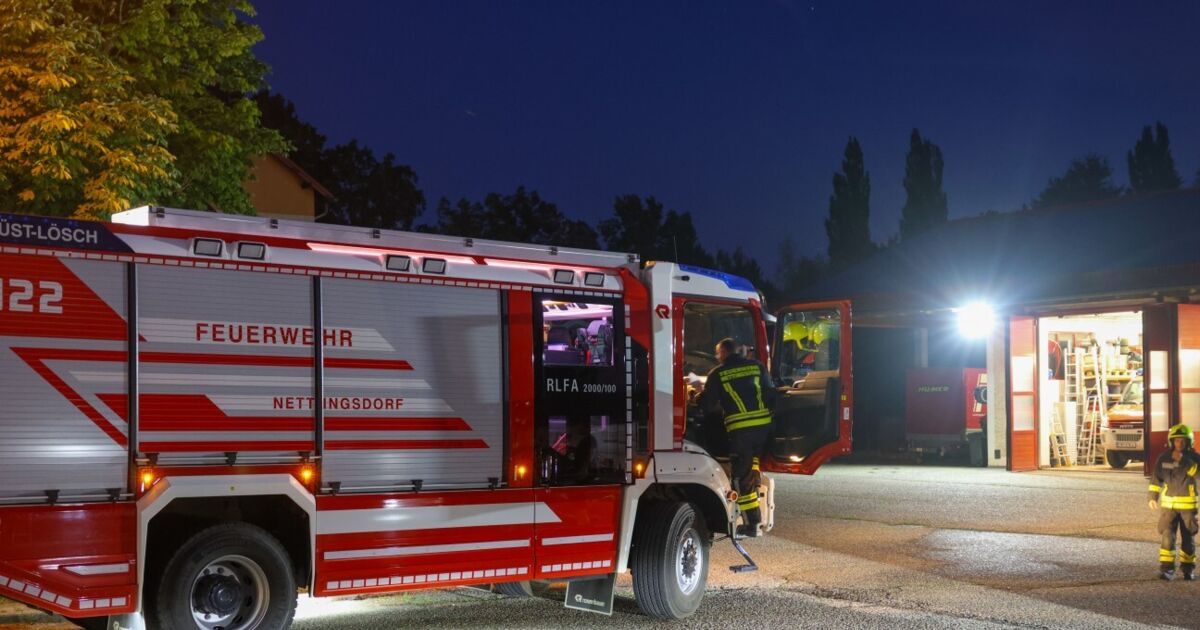A firefighter in protective gear is entering a fire truck, the lights are on, and it is nighttime.