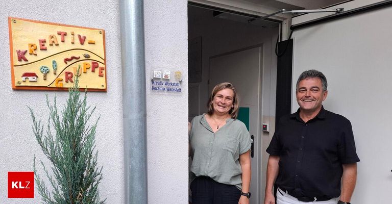 Two individuals stand outside a building with a sign that reads Kreativ Werkstatt Keramik Werkstatt. The woman wears glasses and a necklace.