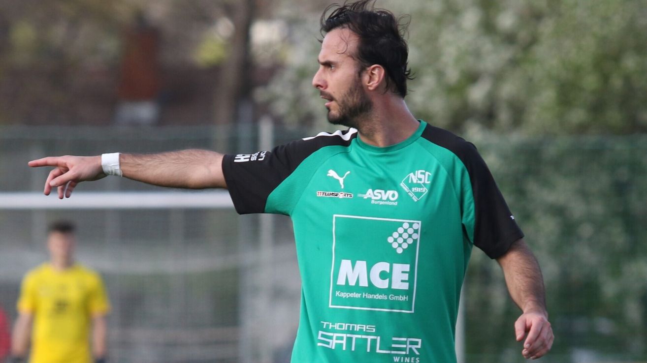 A man wearing a green jersey with the letters MCE, black sleeves, and a logo on his chest, standing outdoors.