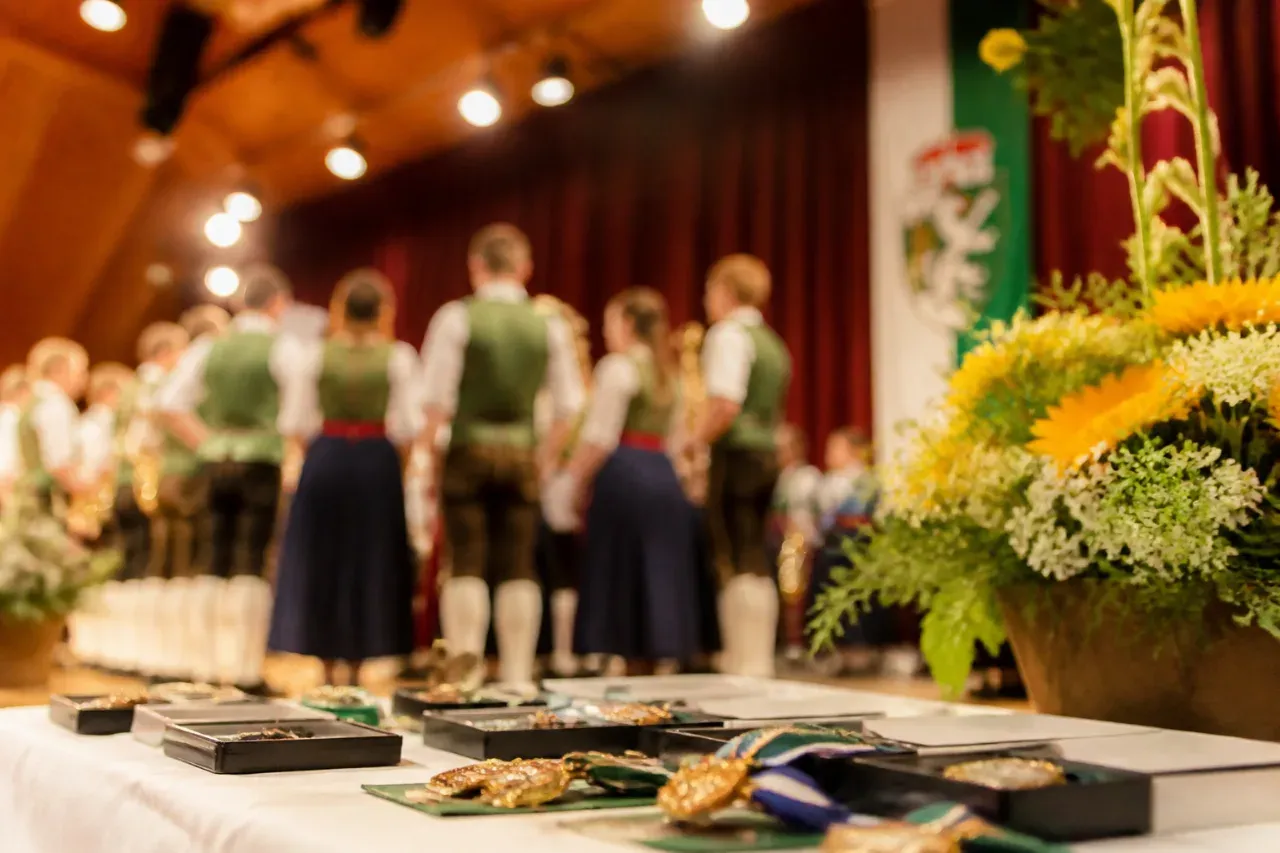 A stage with medals on display in front of a group of people wearing traditional green attire. They stand in a line behind a table adorned with a yellow and white floral arrangement.