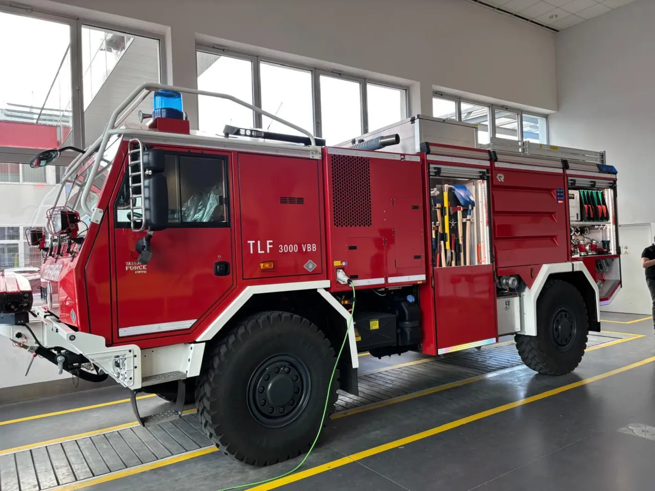 A large red fire truck with the text TLF 3000 VB8 on the side is parked in a garage.