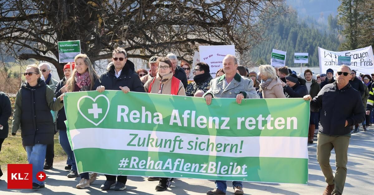Protesters hold a banner with the text 'Reha Aflenz retten Zukunft sichern!' and a hashtag. They are standing outside with mountains in the background.