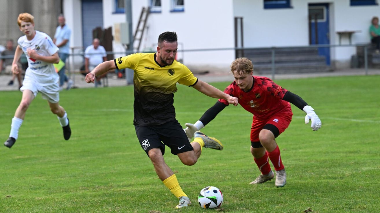 Two soccer players compete on a field, one in yellow and black, the other in red, both focused on the ball.