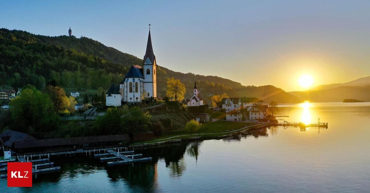 A picturesque village with a church on a hill, surrounded by mountains and a serene lake at sunset.
