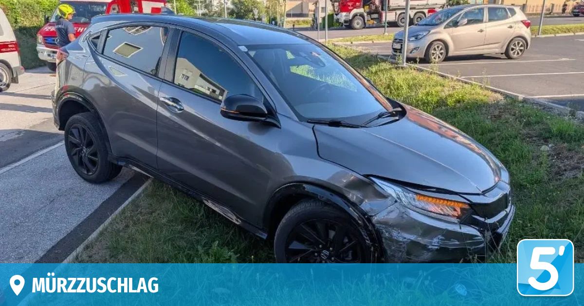 Ein grauer Honda CR-V ist auf einem Rasen geparkt mit sichtbaren Schäden am vorderen Stoßfänger und Seitenspiegel. Dahinter ist ein weiteres Auto auf der Straße geparkt.