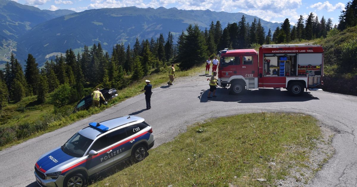 Ein Polizeiauto ist am Straßenrand geparkt, wo ein umgekippter Wagen steht und Rettungskräfte ihn inspizieren.