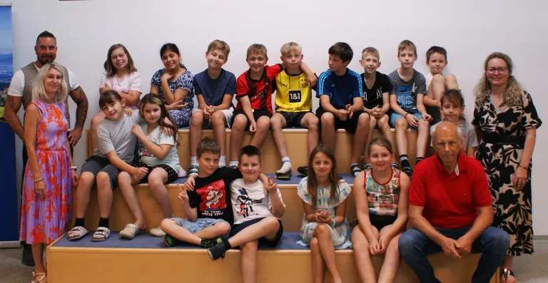 A group of children sitting on bleachers, some wearing sports jerseys, smiling for a photo.