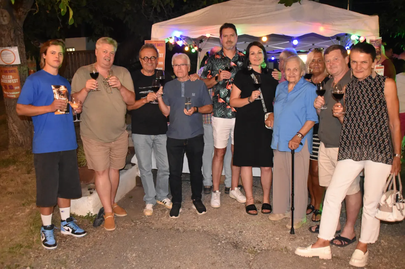 A group of people are standing under a tent, holding wine glasses and smiling for a photo.