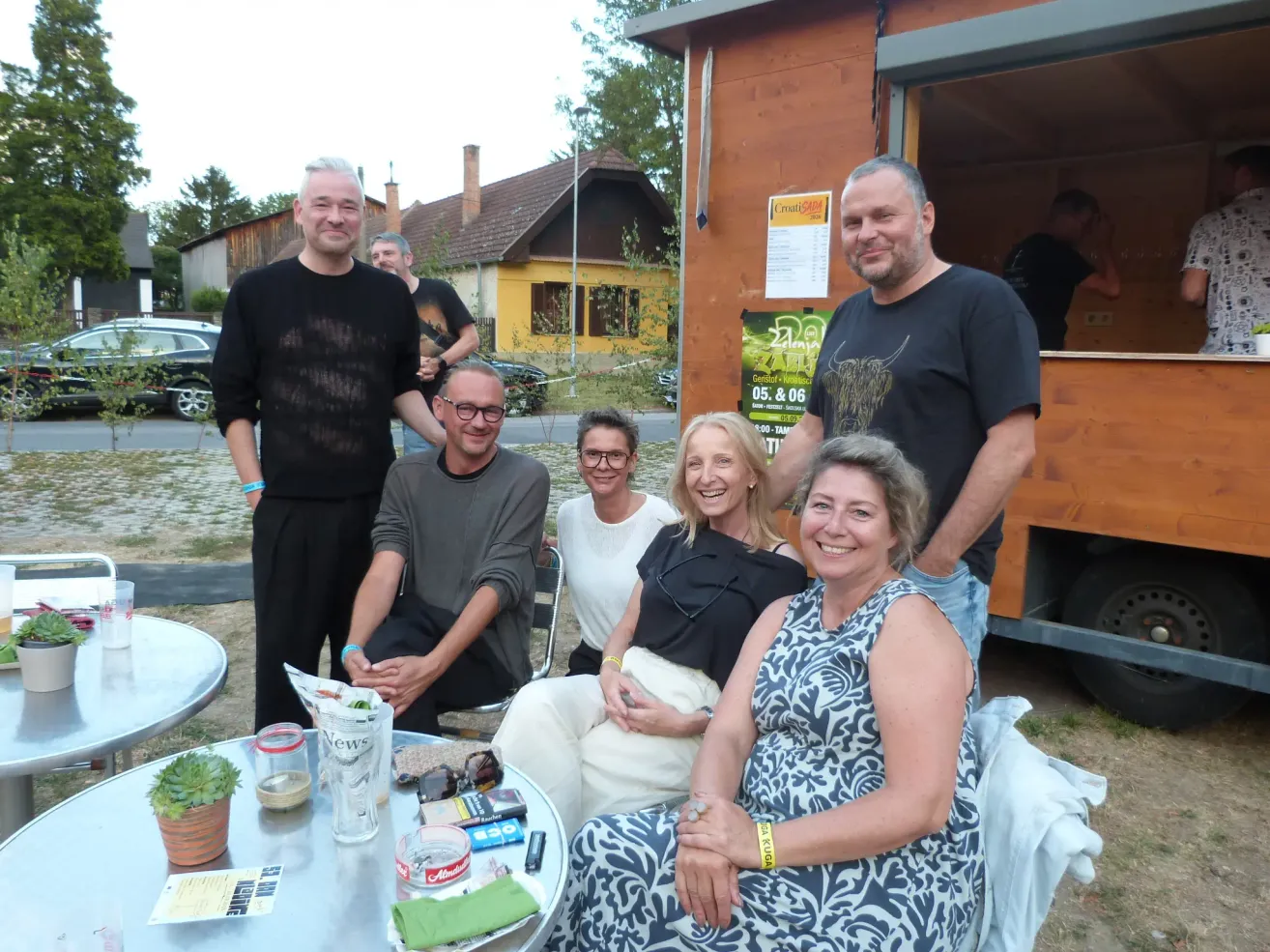 Eine Gruppe von Menschen lächelt und posiert für ein Foto im Freien in der Nähe eines Imbisswagens und eines Hauses.