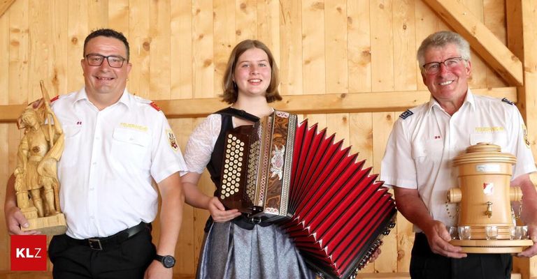 Three people stand in front of a wooden wall. The woman in the middle holds an accordion, while the two men on either side wear uniforms.