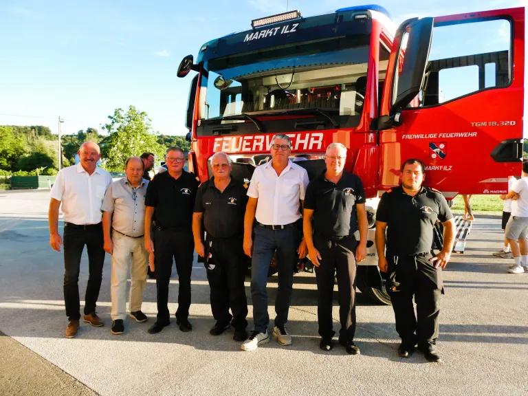 A group of men, dressed in black and white, stand in front of a red fire truck. They are all smiling and appear to be posing for a photo.