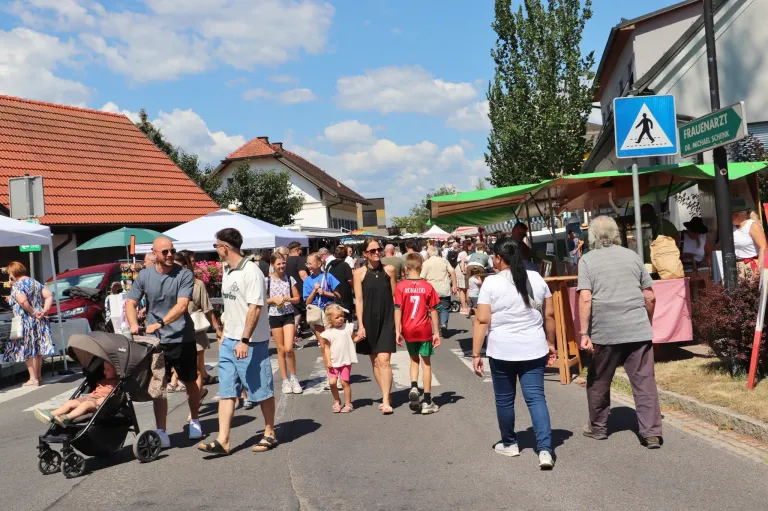 A bustling street market with people walking, some wearing sunglasses and sneakers, and a child in a red shirt with the number 7.