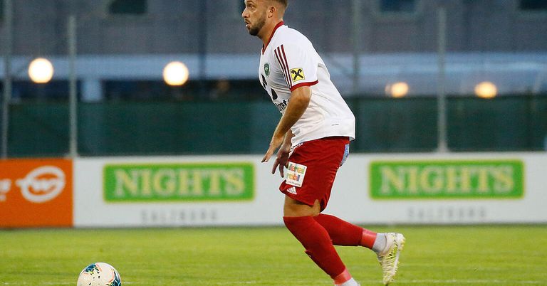 A soccer player in a white and red uniform runs on the field, looking towards the ball.