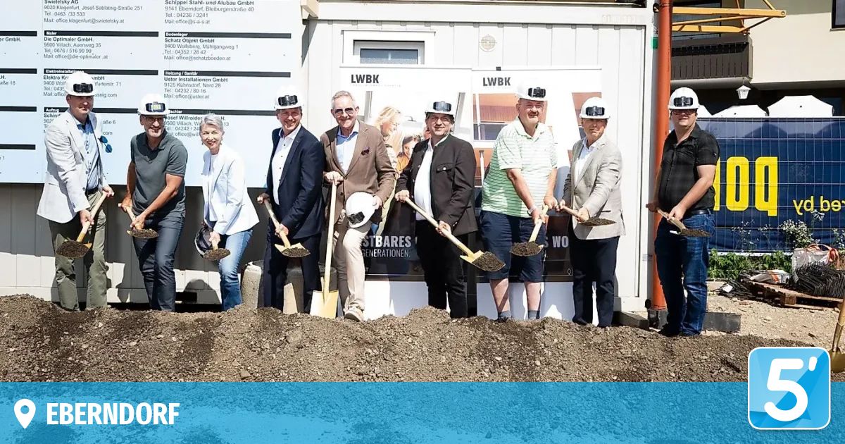 A group of people in hard hats and shovels are standing in front of a building during a groundbreaking ceremony.