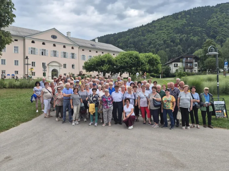 Eine große Gruppe von Menschen, wahrscheinlich Touristen, posiert für ein Foto vor einem großen Gebäude mit einem Berg im Hintergrund.