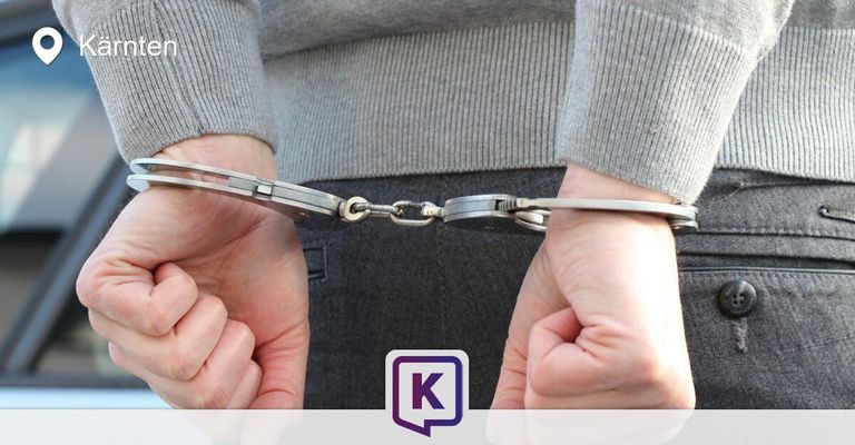 A person's hands are handcuffed in front of them, with a logo in the bottom right corner.