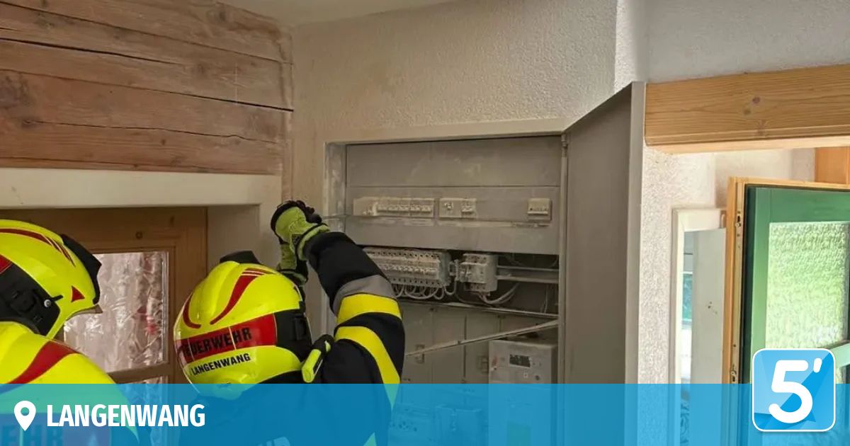 Ein Feuerwehrmann in voller Ausrüstung arbeitet an einem Stromverteiler in einem Gebäude. Der Verteiler ist geöffnet, und der Feuerwehrmann justiert oder überprüft die Verkabelung.