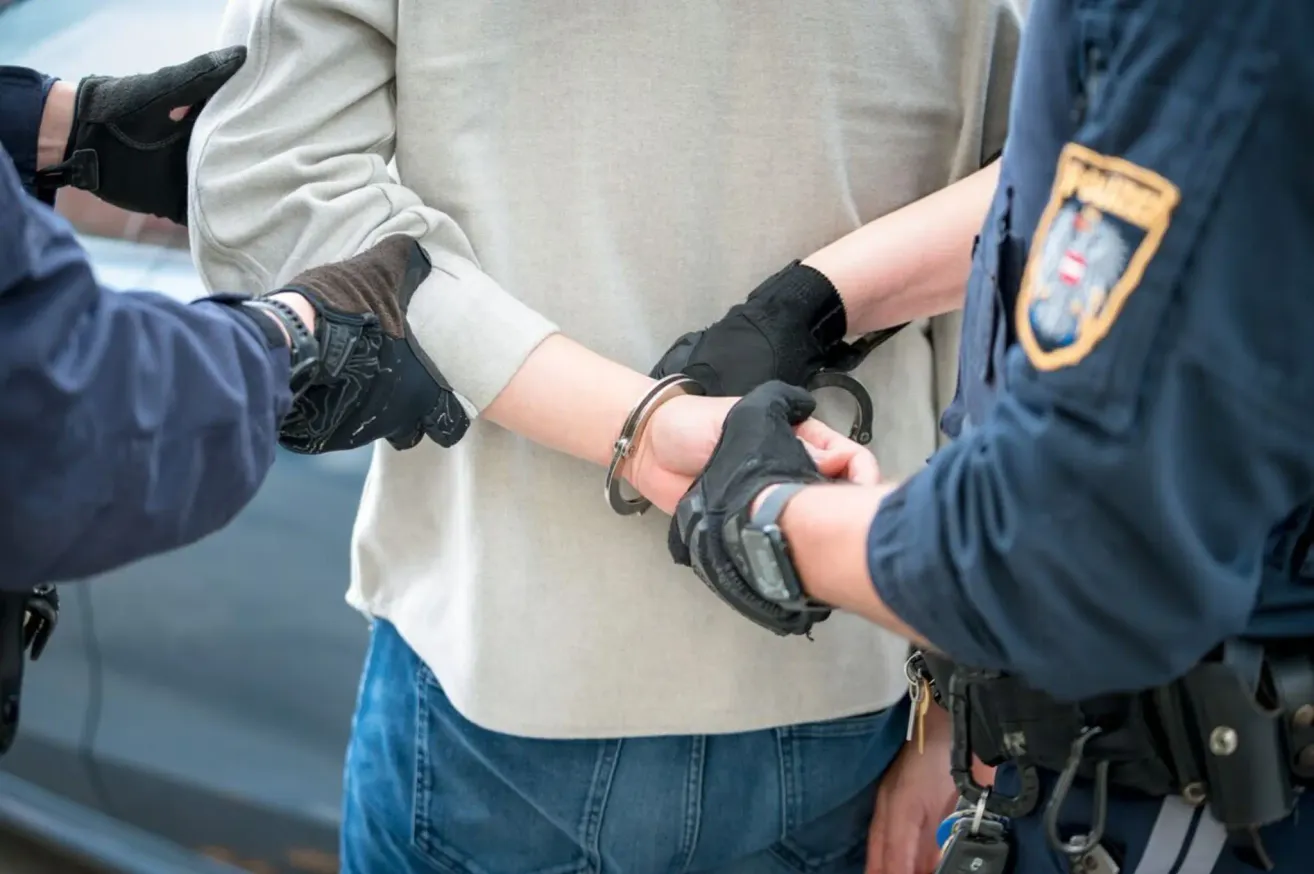 A person in handcuffs is being escorted by two police officers, one holding their left arm and the other holding their right.