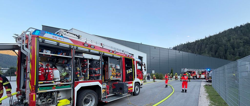 A fire truck labeled BW 40/1 is parked in front of a building with firefighters in red uniforms attending to a hose.