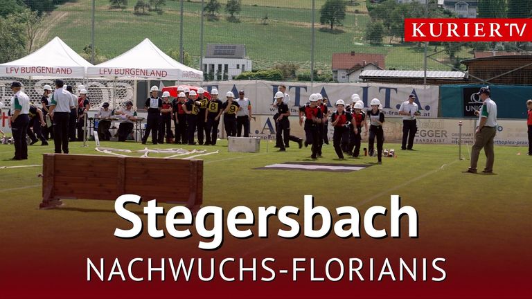 Eine Gruppe von Personen in weißen Helmen und nummerierten Trikots läuft auf einem Feld mit einem weißen Zelt und einem Banner im Hintergrund.