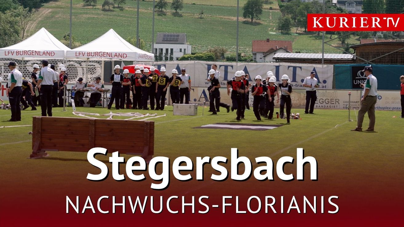 Eine Gruppe von Personen in weißen Helmen und nummerierten Trikots läuft auf einem Feld mit einem weißen Zelt und einem Banner im Hintergrund.