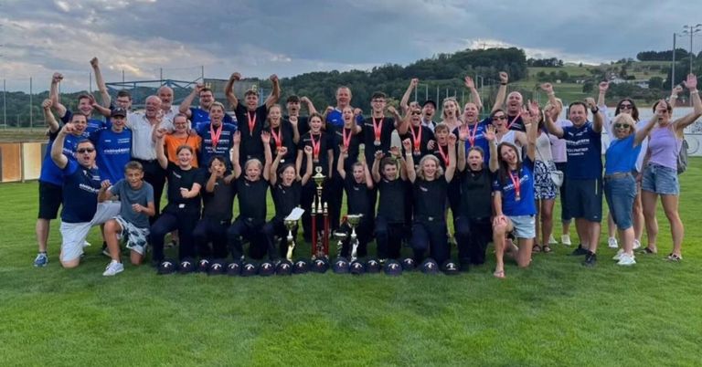 A group of people, possibly a sports team, are posing for a photo with their medals and trophies on a grassy field.