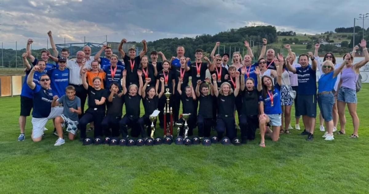 Eine Gruppe von Menschen, wahrscheinlich ein Sportteam, posiert für ein Foto mit ihren Medaillen und Trophäen auf einem Rasenfeld.