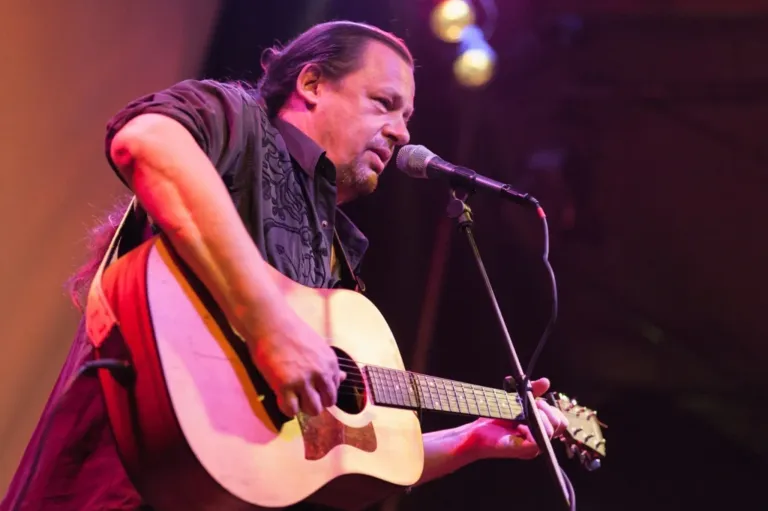 A man with long hair is playing a guitar and singing into a microphone on stage.