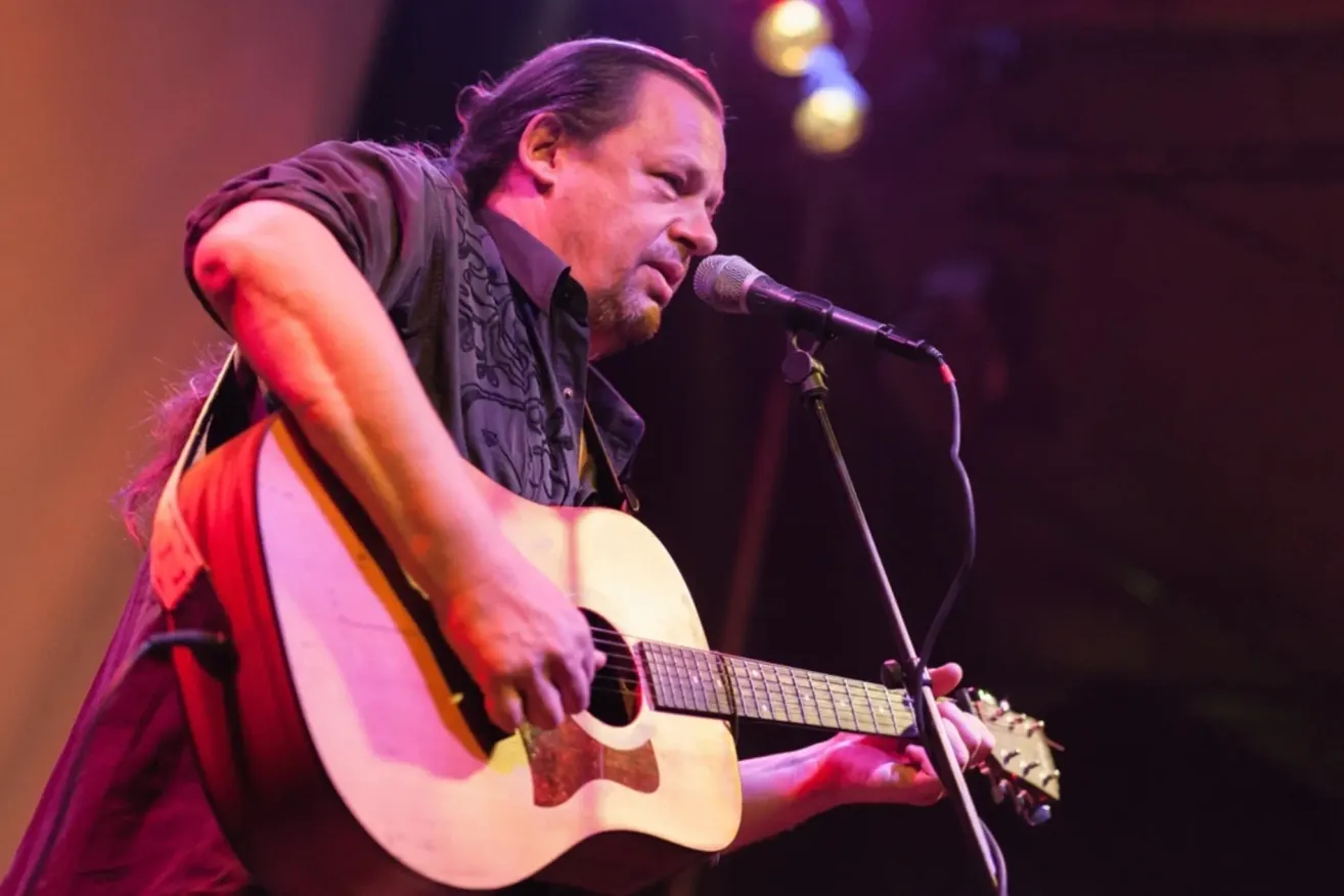 A man with long hair is playing a guitar and singing into a microphone on stage.