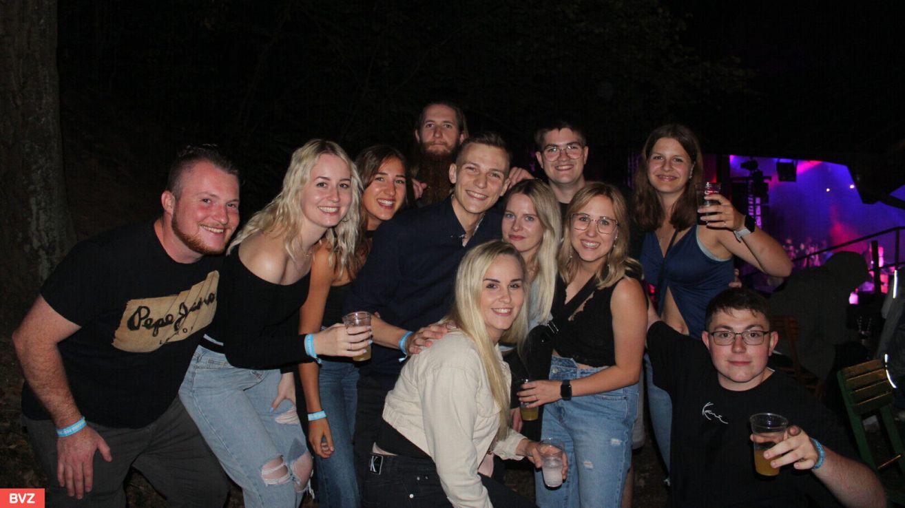 Eine Gruppe junger Erwachsener lächelt und posiert für ein Foto bei Nacht. Einige halten Getränke.