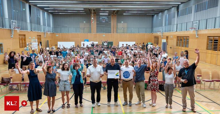 Group photo of people in a sports hall, some holding signs with the text 'klima+energiefonds', raising their hands and posing for the camera.
