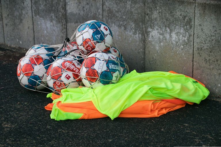 Mehrere Fußballbälle in verschiedenen Farben und Designs sind in einem Netz. Sie werden wahrscheinlich für ein Spiel verwendet. Ein grüner und orangefarbener Stoff liegt auf dem Boden.